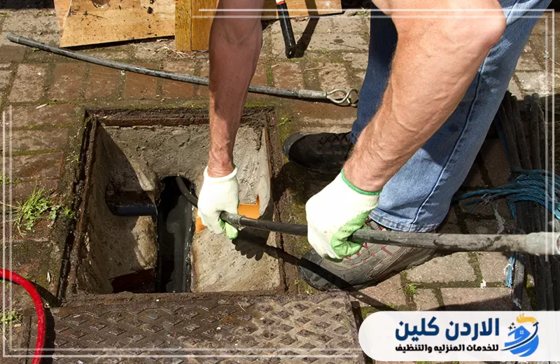 فني يعالج انسداد فتحة صرف خارجية باستخدام أدوات التسليك اليدوية المرنة.