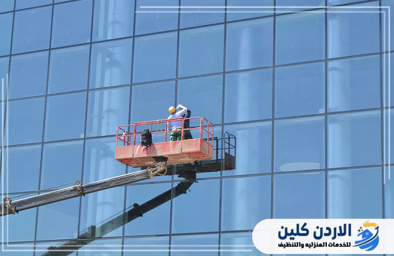 احجز تنظيف واجهة شركتك في الأردن اليوم 0798779667. عامل ينظف زجاج واجهة منشأة تجارية باستخدام رافعة متحركة للوصول إلى أجزاء الواجهة الخارجية.
