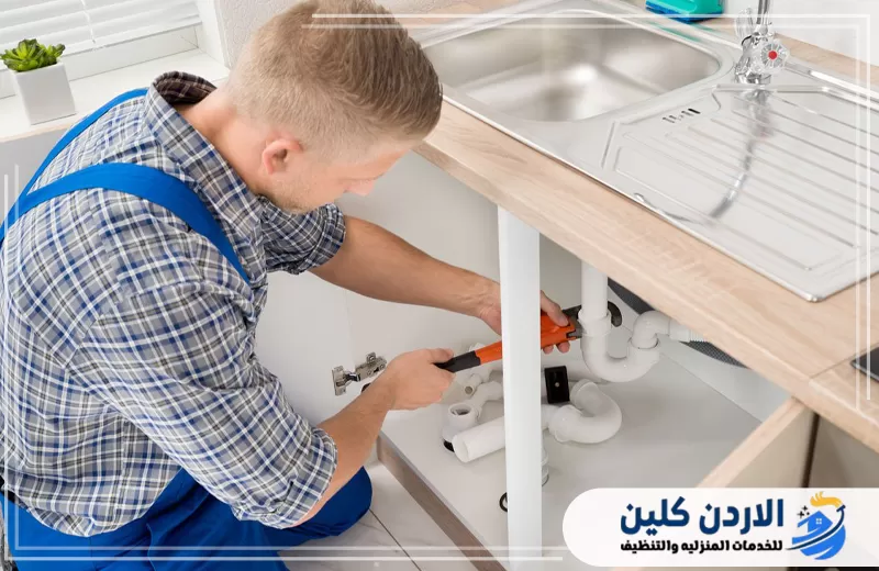 سباك يعمل تحت مجلى المطبخ لإصلاح التوصيلات البلاستيكية ومعالجة مشكلة الصرف أسفل الحوض.
