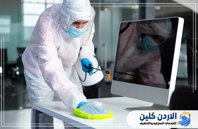 عامل يقوم بمسح وتعقيم المكتب وسطح العمل وأجهزة الكمبيوتر ضمن خدمة تعقيم المكاتب في الأردن.