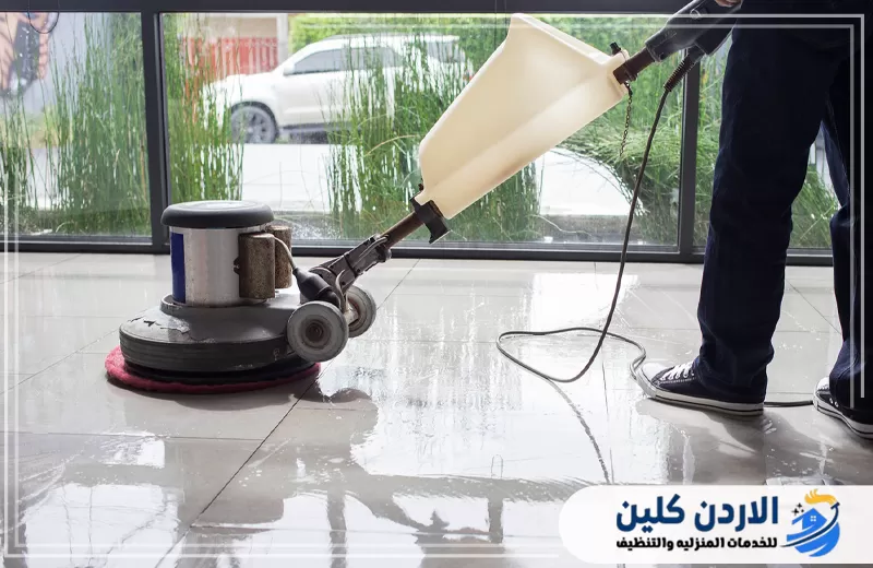 عامل يستخدم ماكينة تنظيف وجلي على أرضية مبللة لإزالة الأوساخ والرواسب وتحسين لمعان البلاط.