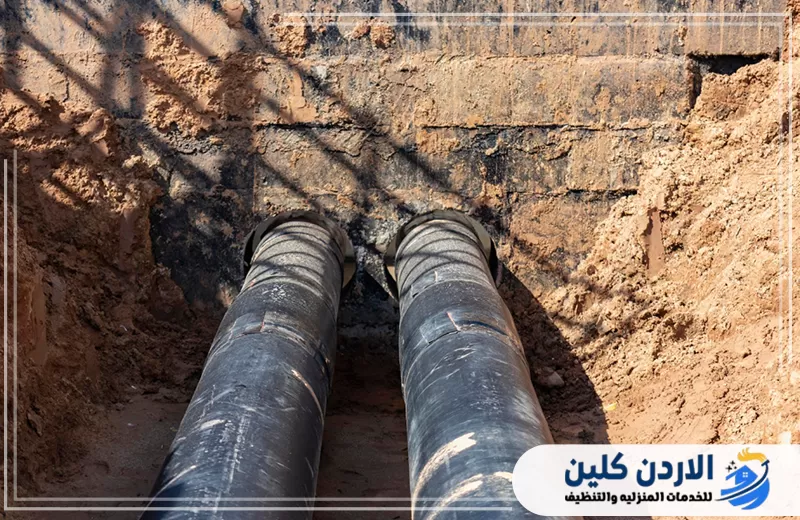 خطان كبيران من مواسير المياه السوداء ممتدان داخل حفرة أرضية وداخلان عبر جدار خرساني ضمن أعمال تأسيس شبكة المياه.