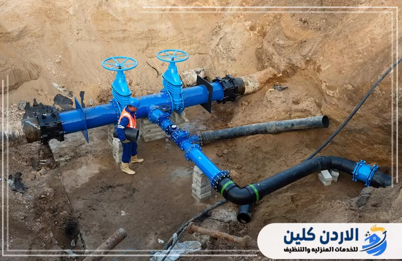 فني يقف بجوار شبكة مياه رئيسية مزودة بمواسير كبيرة ومحابس زرقاء للتحكم في تدفق المياه وتوزيعها.