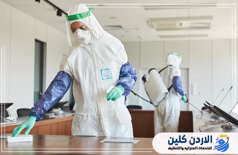 فريق تعقيم يرتدي معدات وقاية ويقوم بتطهير المكاتب والطاولات داخل بيئة عمل إدارية.